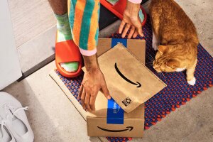 Person opening Amazon packages with orange sandals and colorful socks, cat nearby