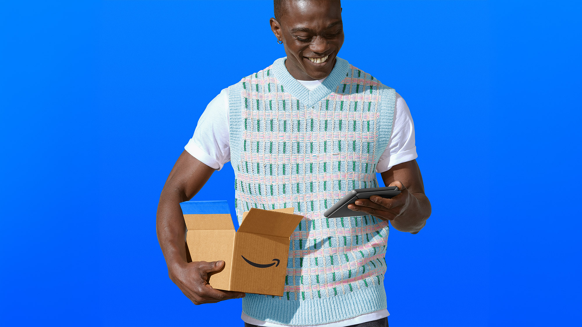 Smiling person holding Amazon package and device against blue background