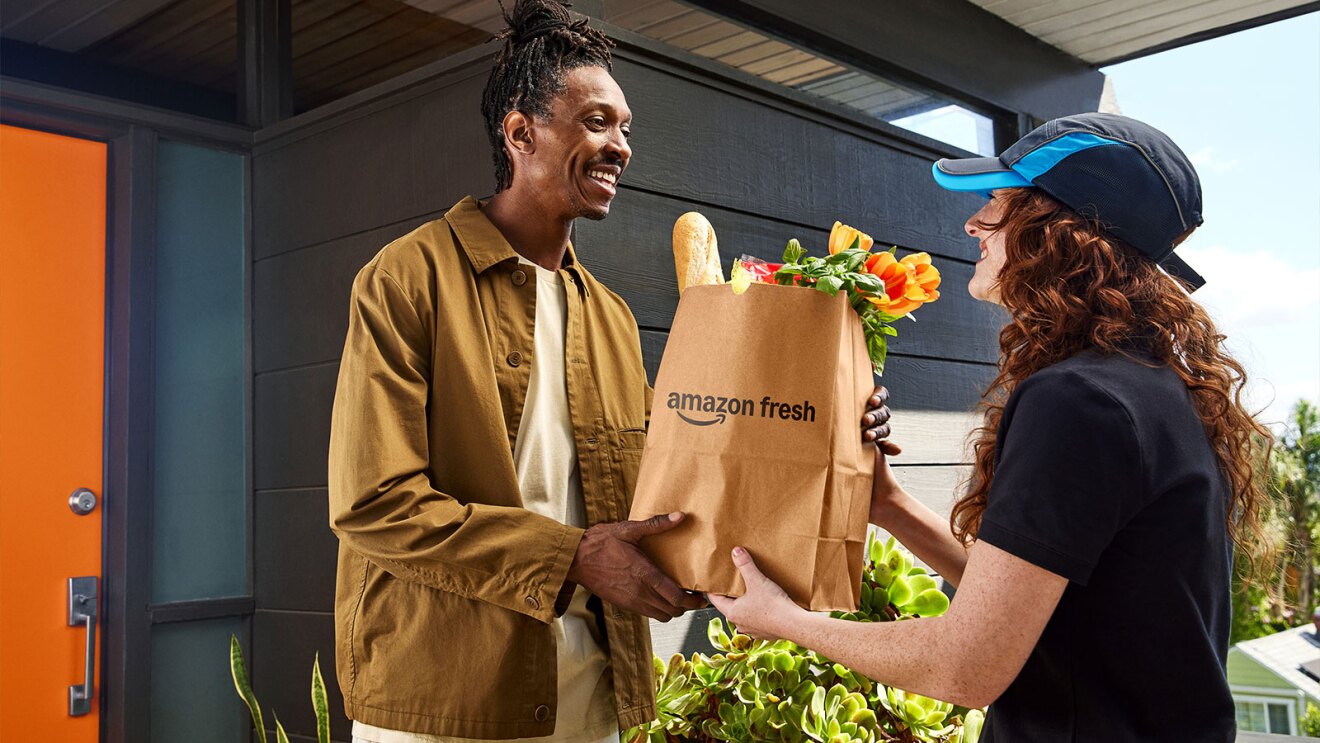Amazon Fresh delivery person handing grocery bag to smiling customer at doorstep