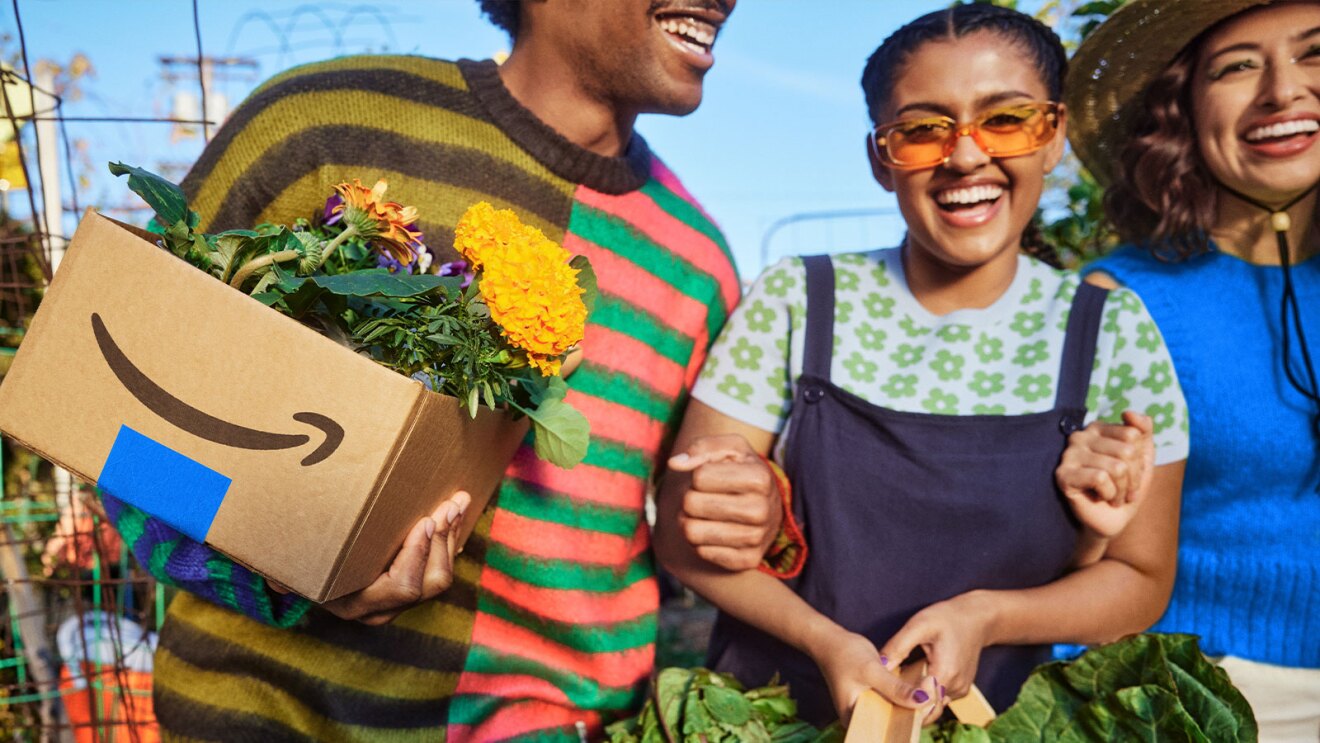 Friends smiling with Amazon box filled with flowers and produce