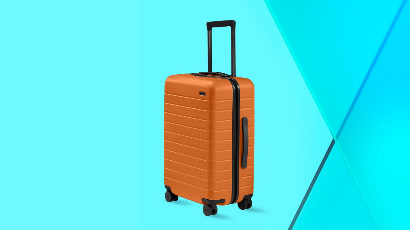 Orange hardshell suitcase on wheels against turquoise background