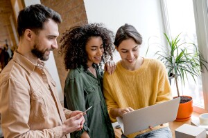 Three professionals gathered around laptop in bright space