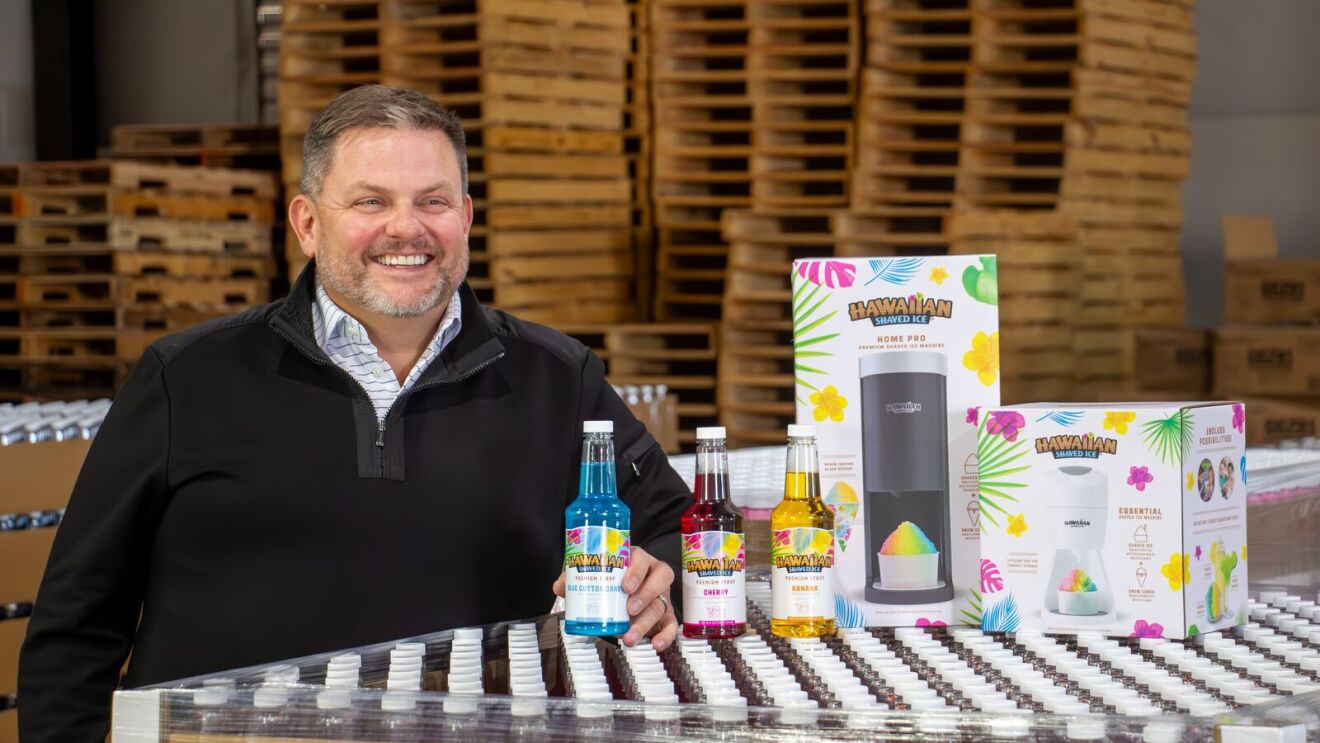 Smiling man displaying Hawaiian shaved ice products in warehouse