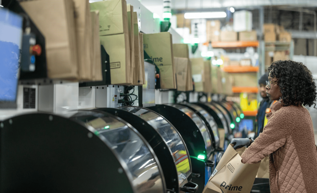 Employee with Prime bag observing automated sorting system in warehouse