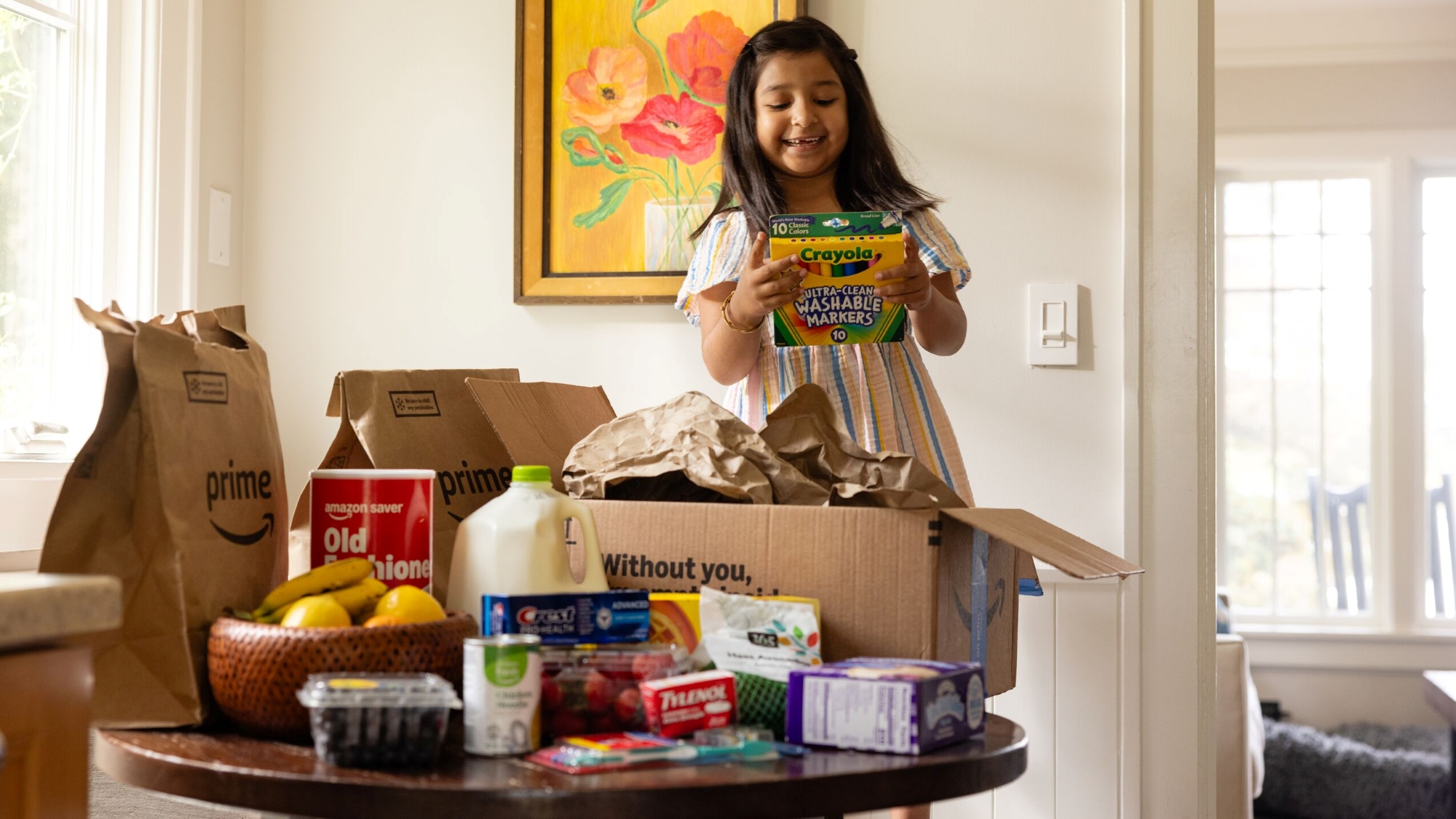 Child smiling with Crayola markers amid Amazon Prime delivery boxes and groceries