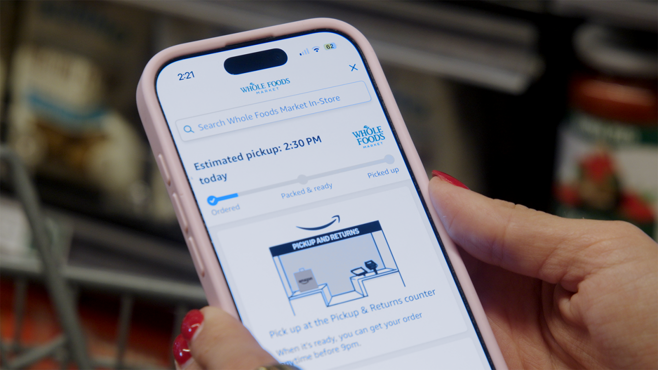 Hand holding smartphone displaying Whole Foods Market app in grocery aisle
